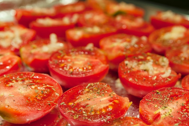 Red halves juicy tomatoes with spices on a baking sheet before drying