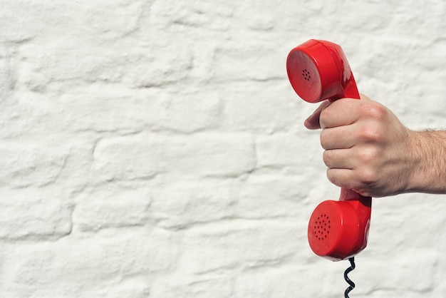 red handset in hand on a brick wall background