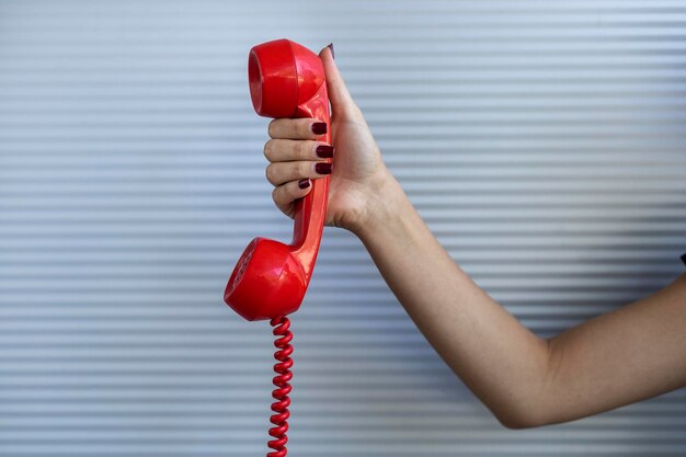 Красный телефон в женской руке серый фон концепция винтажных технологий
