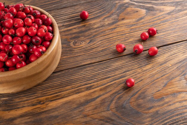 Red hawthorn berries in wooden bowl on flat wooden surface