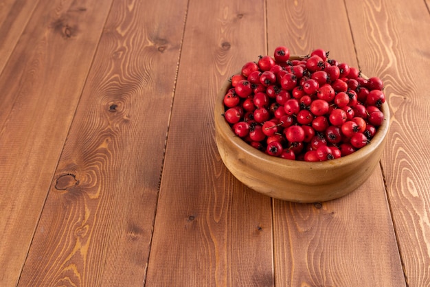 Red hawthorn berries in wooden bowl on flat wooden surface