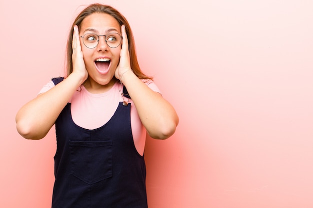 red head girl in an overall excited and surprised looking to the side with both hands on face