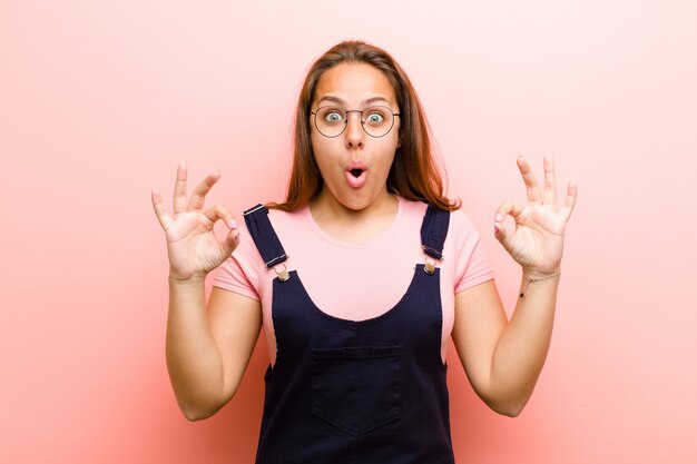 red head girl in an overall feeling shocked and surprised showing okay sign with both hands