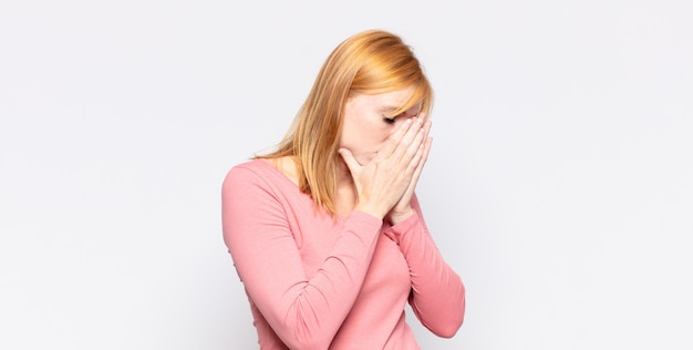 red head pretty woman covering eyes with hands with a sad, frustrated look of despair, crying, side view