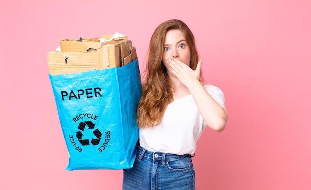 Red head pretty woman covering mouth with hands with a shocked and holding a recycled paper bag