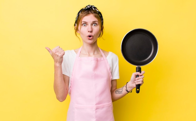 Red head pretty woman looking astonished in disbelief fry pan and housewife concept