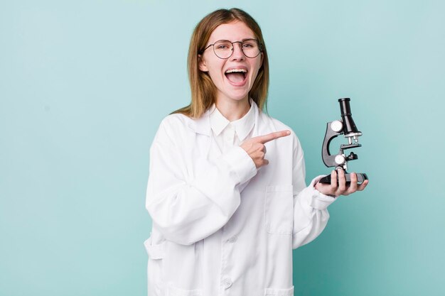 Red head pretty woman looking excited and surprised pointing to the side scientist with microscope concept