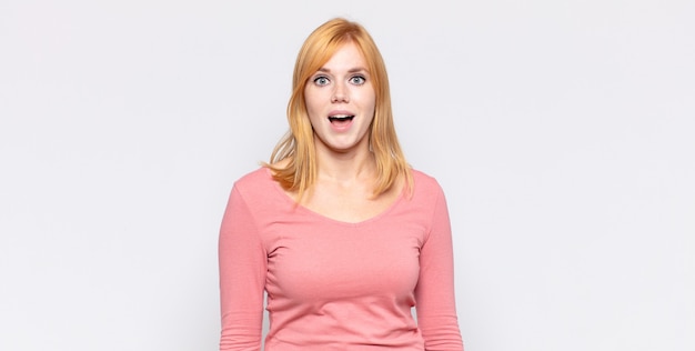 Red head pretty woman looking happy and pleasantly surprised, excited with a fascinated and shocked expression