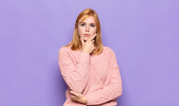 red head pretty woman looking serious, thoughtful and distrustful, with one arm crossed and hand on chin, weighting options