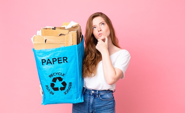 Red head pretty woman thinking, feeling doubtful and confused and holding a recycled paper bag