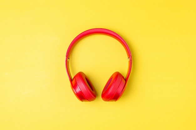 Red headphones listens to music on smartphone over yellow background.