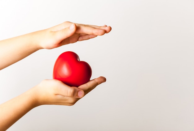 Red heart in child's hands on light background