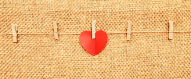 Red heart on clothes pin on brown textile background