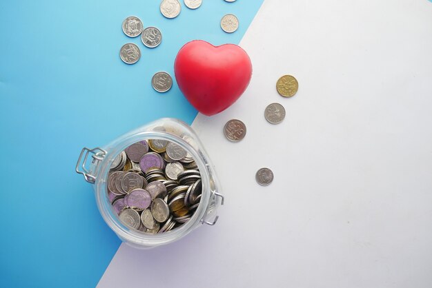 Photo red heart and coins in a jar on color background