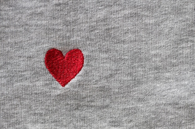 Photo red heart embroidered with threads on gray fabric background close-up macro copy space flat lay