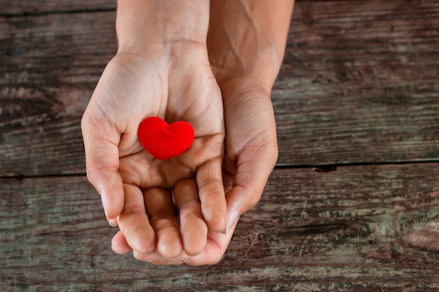 Red heart in female hand on wooden background.