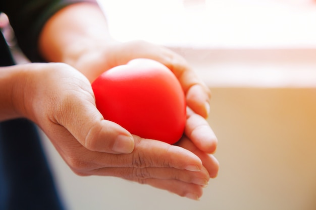 Red heart in female's both hands in black suit background, represents helping hands