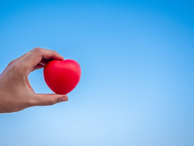 Red heart in hand on blue sky