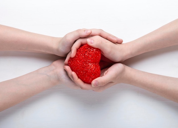 Red heart in the hands of a boy and a girl on a white background