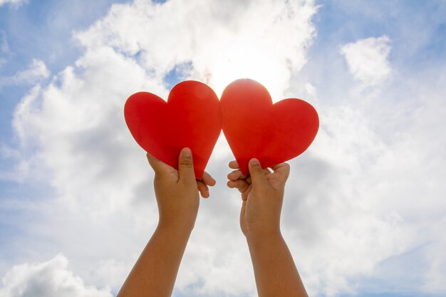 Red heart in hands on sky background