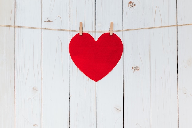 Red heart hanging at clothesline on wood white background with space. Valentine Day.