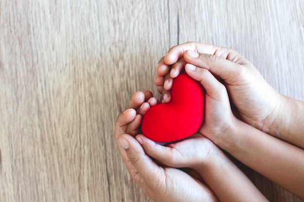 Фото Красное сердце в руках ребенка и родителей руки на фоне деревянный стол с любовью и гармонией