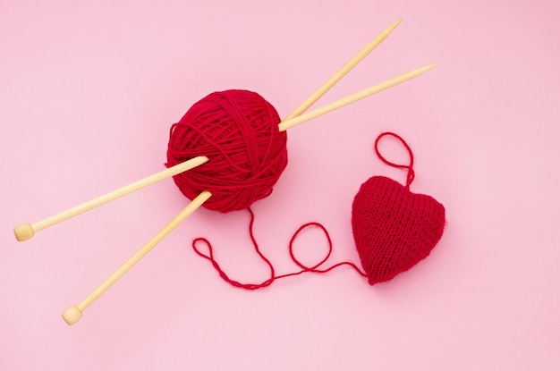 Red heart knitted of yarn a ball of red yarn and knitting needles on a pink background