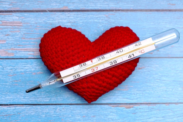 Red heart lies on a blue wooden surface with a thermometer. Cardiovascular health concept. High quality photo