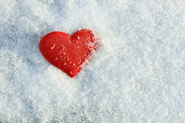 Red heart lying on snow background in sunny winter day