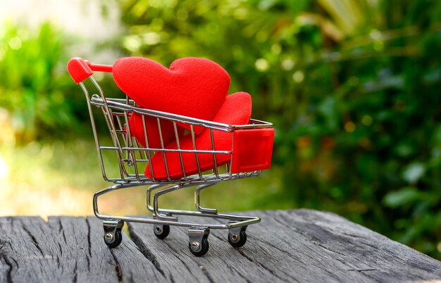 Red heart in mini shopping cart on wooden