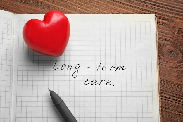 Red heart and notebook with text longterm care on wooden background