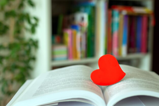 Red heart on open book on background of blurred shelves with
books in library world book lovers day