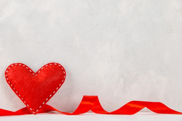 Red heart, ribbon against the of a white wall, concept, a postcard for Valentine's Day.