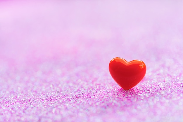 A forma di cuore rosso sulla superficie glitter rosa chiaro astratta