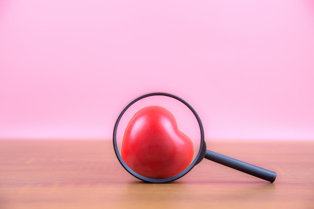 A red heart shaped balloon on the table with a pink background.