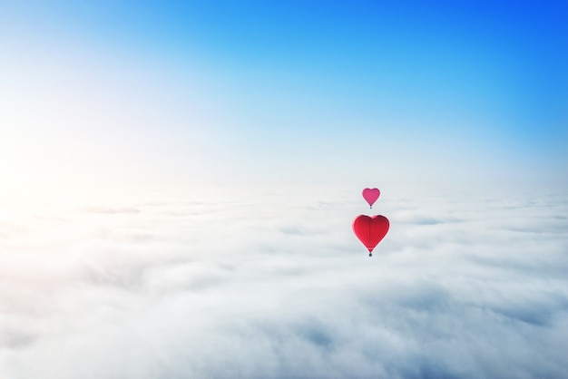 Red heart-shaped balloons in the blue sky over white clouds and the sun