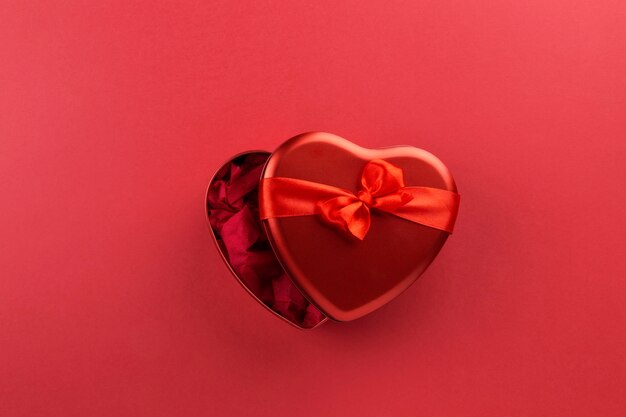 Red heart-shaped box with ribbon on red background