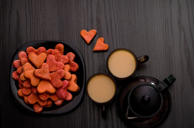 Red heart-shaped cookies, two cups of tea with milk and teapot. Valentine's Day, Copyspace