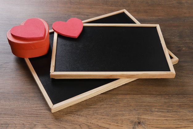 Red heart-shaped gift box and blackboard on wooden table.