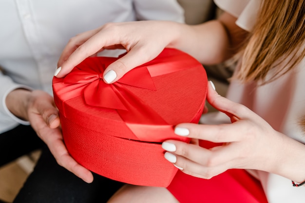 Red heart shaped gift box in hands of woman and man