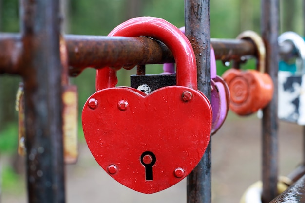 A red heart-shaped padlock hanging on a fence.