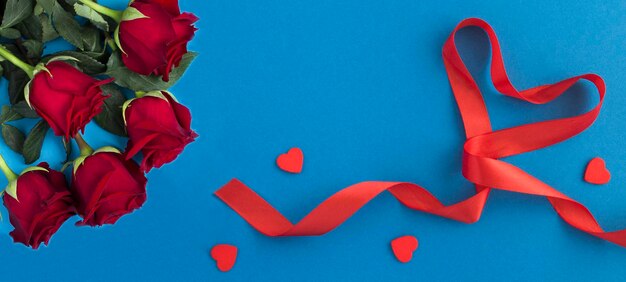 Red heart shaped ribbon and red roses on the blue background Top view Copy space