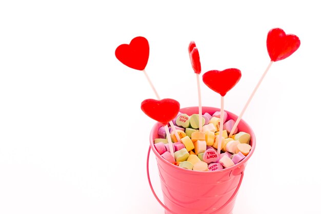 Red heart shaped strawberry lollipops in pink bucket.