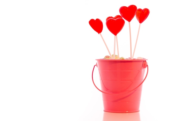 Red heart shaped strawberry lollipops in pink bucket.