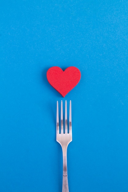 Red heart and silver fork on the blue background. Copy space.Top view.