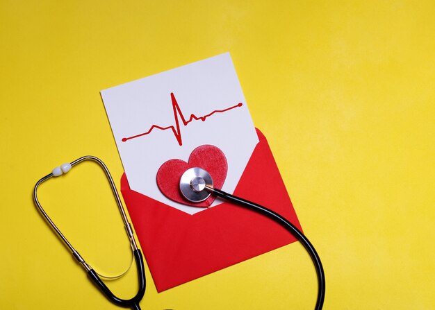 Red heart and stethoscope on white paper with heart chart  in red envelop on a yellow background