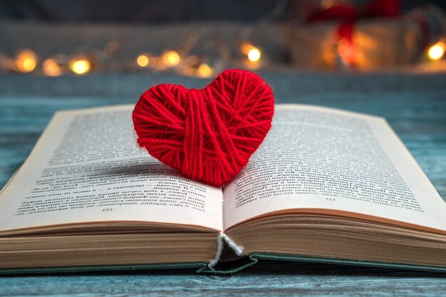 Red heart of thread in an open book on a festive background.