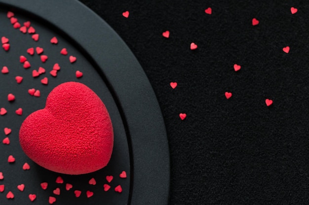 Torta di velluto a cuore rosso su sfondo nero con tante mini caramelle a forma di cuoricini
