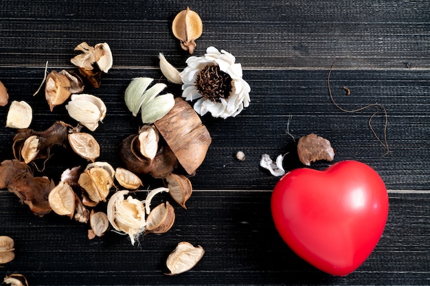 The red heart whit dried leaves and flower is placed on the left side of the black wood table