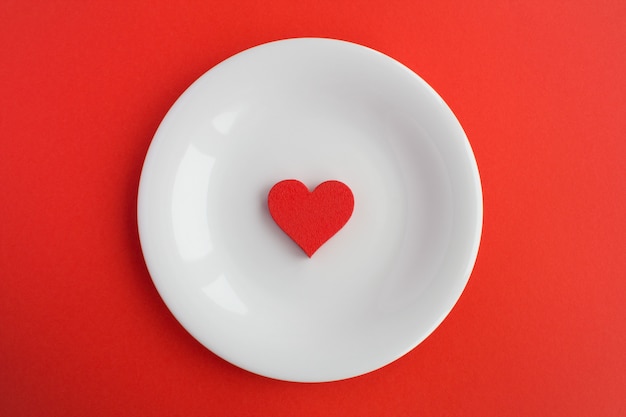 Red heart  on the white plate on the red surface .